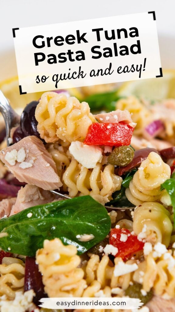 Close-up of Greek tuna pasta salad with rotini, spinach, olives, feta cheese, tuna chunks, red onion, and red bell pepper. A spoon is scooping up a portion.