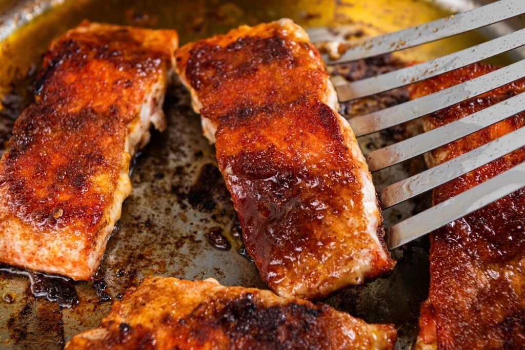 Sweet, savory, and a little smoky, this Pan Seared Salmon is moist and flaky with a caramelized brown sugar crust. Ready in just 15 minutes! Brown sugar salmon fillets cooking in a pan, with a spatula lifting one piece.