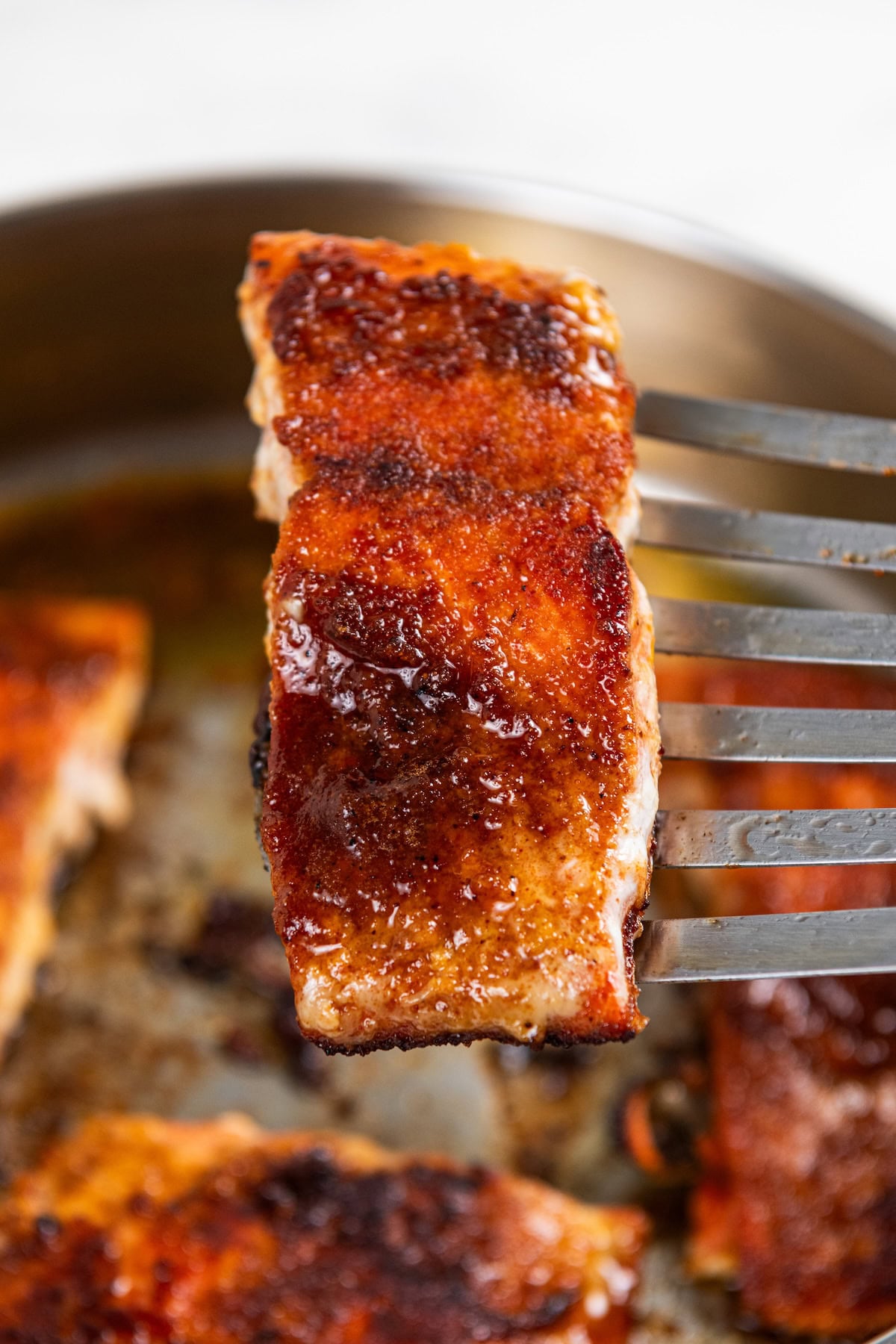 Sweet, savory, and a little smoky, this Pan Seared Salmon is moist and flaky with a caramelized brown sugar crust. Ready in just 15 minutes! A close-up of a spatula holding a pan seared salmon fillet with a caramelized brown sugar crust above a pan with more pieces of salmon in the background.