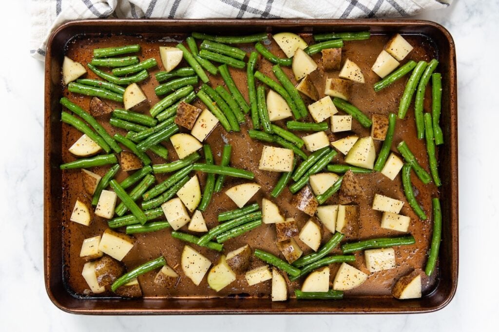 Sheet Pan Steak Bites and Potatoes gives you juicy sirloin, crispy potatoes, and roasted green beans off one pan. Ready in about 40 minutes! A baking sheet with chopped potatoes and green beans seasoned and ready to be roasted.