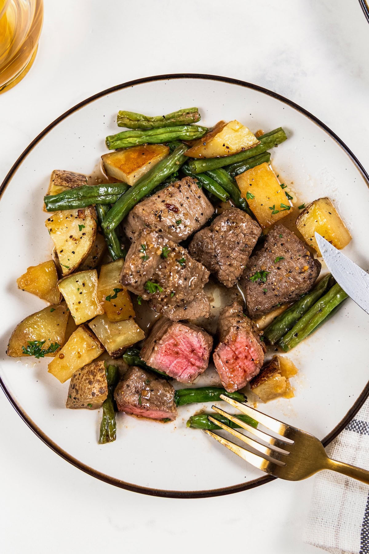 Sheet Pan Steak Bites and Potatoes gives you juicy sirloin, crispy potatoes, and roasted green beans off one pan. Ready in about 40 minutes! A plate with juicy steak bites and potatoes with green beans. Some steak bites are cooked medium-rare and cut open to show the inside. A fork and knife rest on the plate.