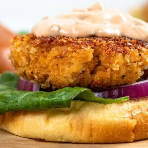 A crispy chicken patty on a bun with lettuce, red onion, and creamy sauce, placed on a wooden board.