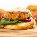 A crispy chicken patty on a bun with lettuce, red onion, and creamy sauce, placed on a wooden board.