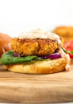 A crispy chicken patty on a bun with lettuce, red onion, and creamy sauce, placed on a wooden board.