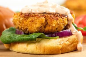 A crispy chicken patty on a bun with lettuce, red onion, and creamy sauce, placed on a wooden board.