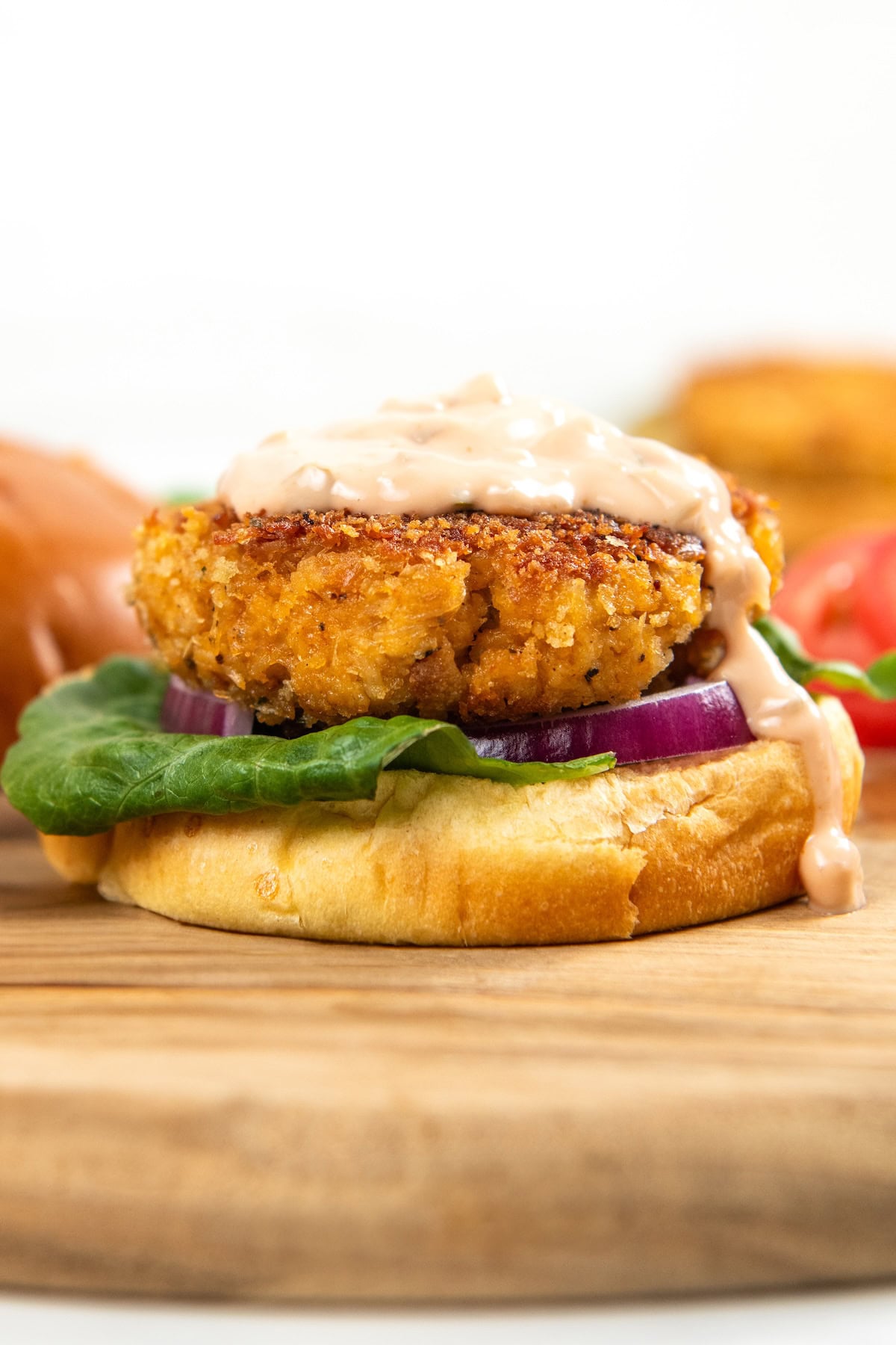 This Chicken Patty Sandwich turns two cans of chicken into a quick and easy dinner for six! Served with a tangy sauce and all the toppings. A crispy chicken patty on a bun with lettuce, red onion, and creamy sauce, placed on a wooden board.