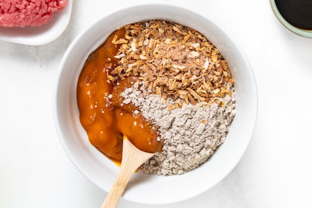 Crockpot Cube Steak is smothered in a rich and thick brown gravy with onions until it's fall-apart tender. Set it and forget it! A white bowl contains dry soup mix, beef gravy mix, and golden mushroom soup being stirred with a wooden spoon.