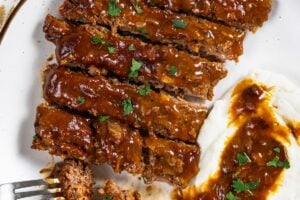 Sliced crockpot cube steak and gravy is served next to mashed potatoes with gravy on a white plate.