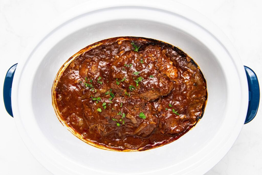 Crockpot Cube Steak is smothered in a rich and thick brown gravy with onions until it's fall-apart tender. Set it and forget it! Slow cooker cube steak and gravy topped with fresh parsley fills the inside of a white crockpot.