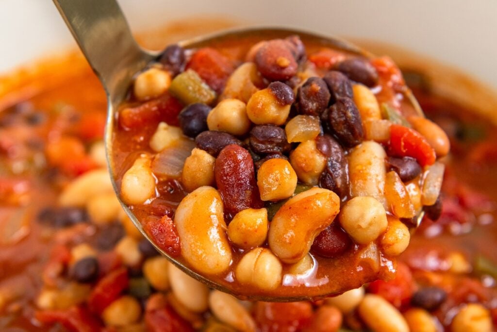 So thick and hearty, this 5 Bean Chili recipe is made in just one-pot with canned beans and a few simple pantry staples. Ready in 30 minutes! A metal ladle filled with a mixture of assorted beans, diced tomatoes, and vegetables in a red broth.
