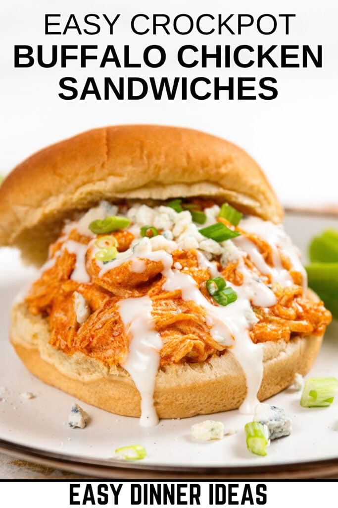 A crockpot buffalo chicken sandwich topped with ranch dressing, blue cheese crumbles, and green onions is served on a bun.