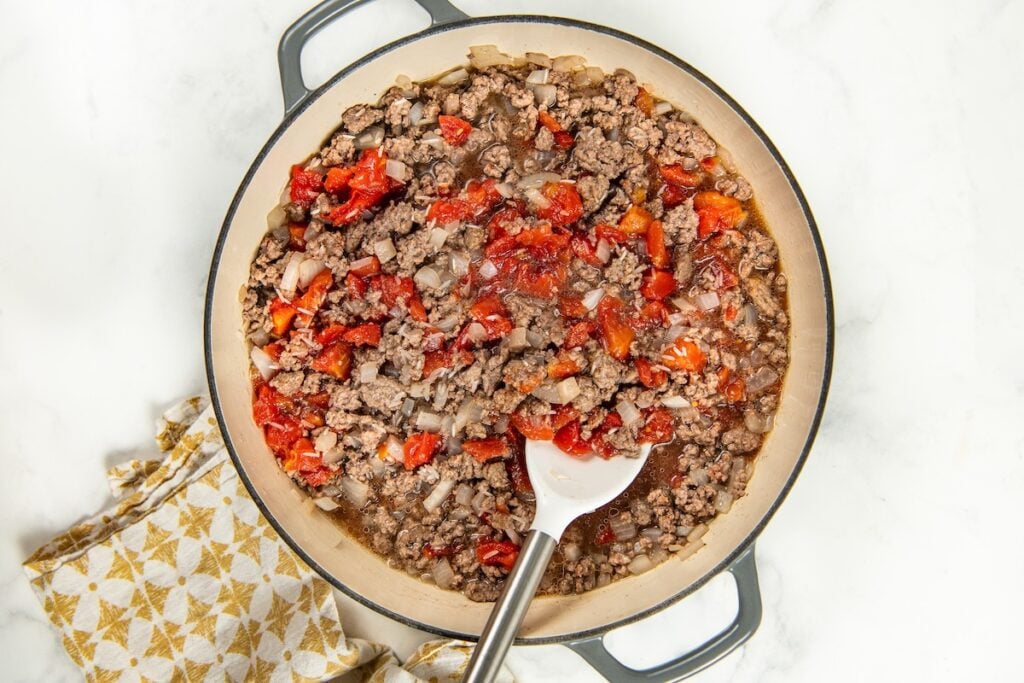 This easy Skillet Beef and Rice recipe is a hearty one-pan recipe that needs no sides. It's a budget dinner the whole family will love! A skillet filled with a mixture of browned ground meat, chopped onions, and diced tomatoes, with a white silicone spatula resting inside.