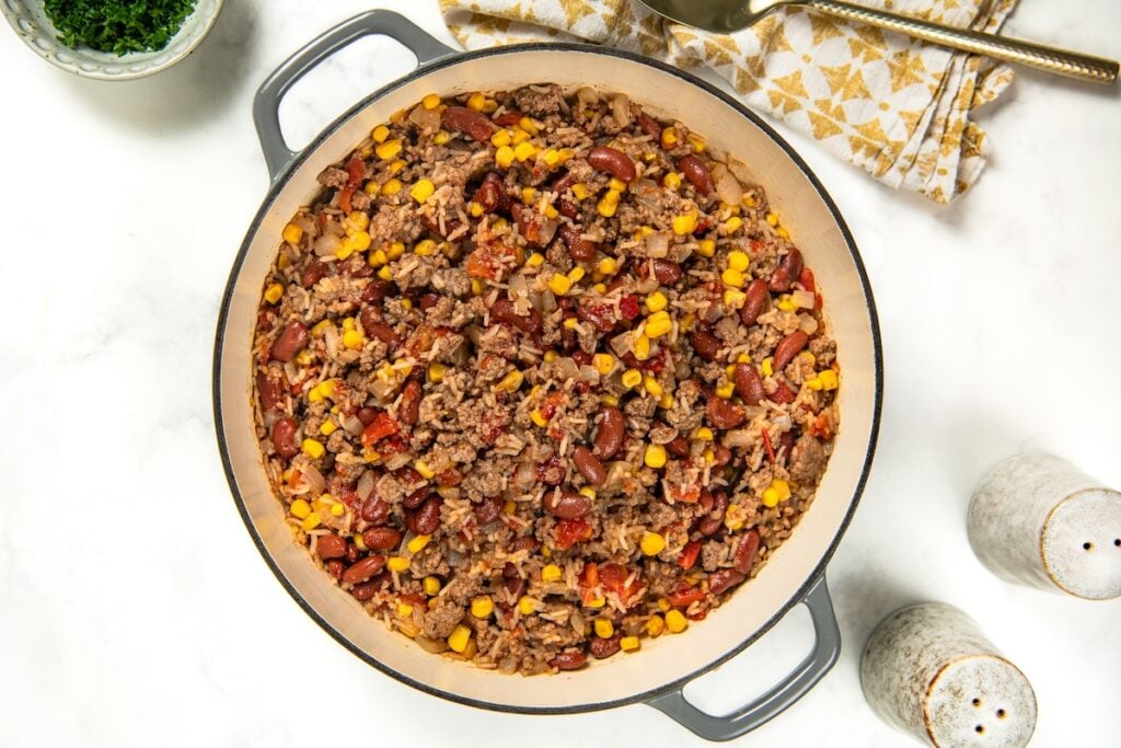 This easy Skillet Beef and Rice recipe is a hearty one-pan recipe that needs no sides. It's a budget dinner the whole family will love! A large skillet filled with a mixture of ground meat and rice with beans, corn, and tomatoes.