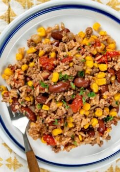 A serving of skillet beef and rice with beans and corn topped with chopped parsley, on a white plate with a fork on the side.
