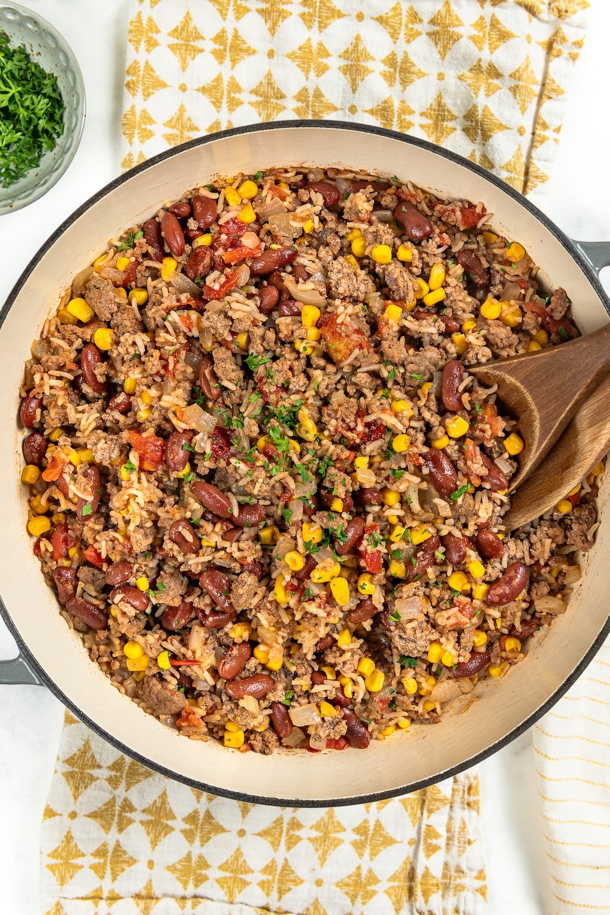This easy Skillet Beef and Rice recipe is a hearty one-pan recipe that needs no sides. It's a budget dinner the whole family will love! A large skillet filled with a mixture of ground meat and rice with kidney beans, corn, and tomatoes, served with a wooden spoon.